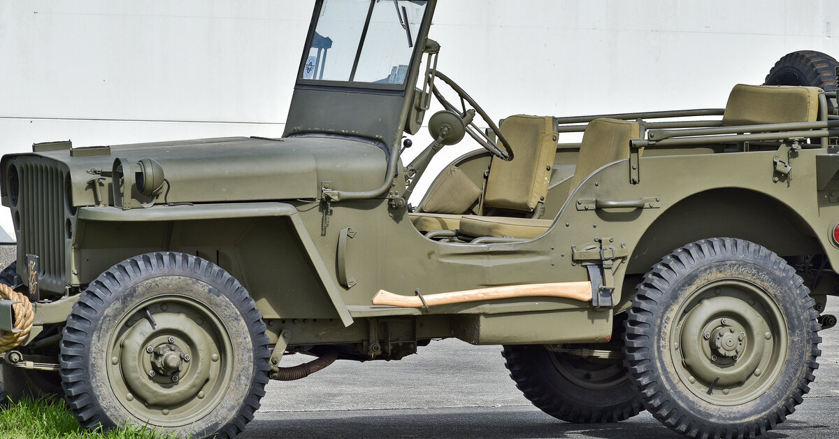 A WWII-era Willys Jeep military vehicle in a classic forest green color parked in a lot next to a building.